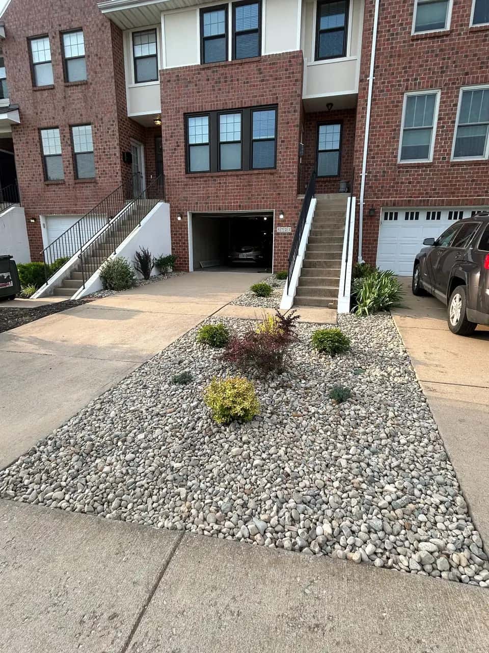 Driveway-side garden bed with river rock and shrubs